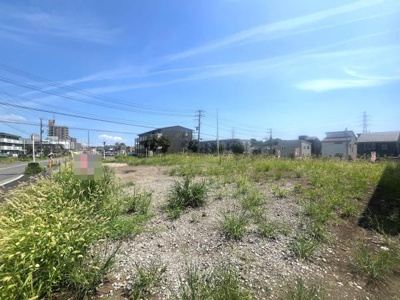 開放感のある現地土地写真です。周囲には住宅が立ち並び街並みに馴染む雰囲気があります。陽当たりが期待できる環境です。道路沿いでアクセスもしやすい立地となっています。