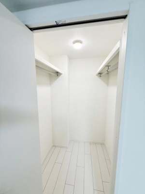 扉を開けると広がる収納スペースは奥行きがあり使いやすい形状です。棚やハンガーパイプが設置されており収納力が充実しています。明るい照明付きで物の出し入れも快適に行えます。床や壁の清潔感も印象的です。