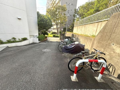 自転車を安心して駐輪できるスペースがあります。敷地内は舗装されており日当たりも良好です。建物と道路の間にゆとりがあり開放感があります。周囲には緑も点在しています。