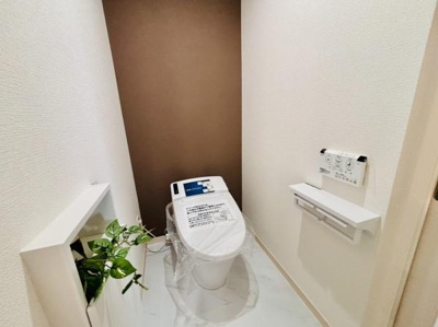 落ち着きのあるアクセントクロスが特徴的なトイレです。手元に便利なペーパーホルダーや操作パネルが設置されています。観葉植物が空間を爽やかに演出しています。ゆったりとしたスペース設計です。