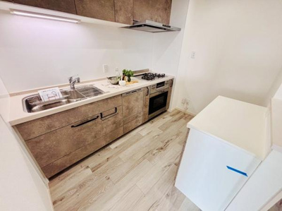 木目調のキャビネットが落ち着いた印象を与えます。ワイドなシンクで水作業もスムーズに行えます。コンロとシンクの配置がバランスよく使いやすいレイアウトです。収納も豊富で整理整頓しやすいキッチンです。