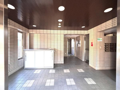 ロビーは明るい照明が天井に配置されています。タイル張りの壁と床が清潔感を感じさせます。郵便受けや設備もすっきりとまとめられています。通路が広く開放感のある造りになっています。