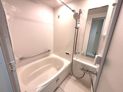 清潔感のあるバスルームです。浴室内には手すりが設置されており安全面にも配慮されています。ミラーと洗い場が広めの設計で使い勝手の良い空間です。シャワーヘッドは高さ調節が可能です。