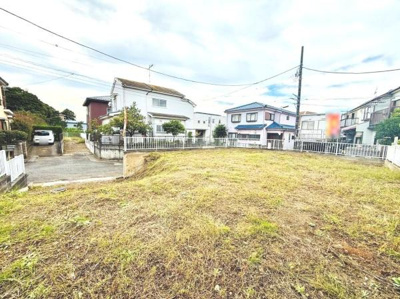 開放感のある現地土地写真です。周囲には住宅が並び落ち着いた環境が魅力的です。敷地には柵が設けられており安心感があります。整地された地面で自由なプランニングが可能です。