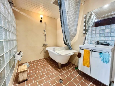 ガラスブロックの壁が特徴的な明るい空間です。洗面台は大きな鏡付きで使い勝手の良さが感じられます。レンガ調のフロアが個性的な雰囲気を演出しています。全体的にゆったりとした配置で開放感があります。