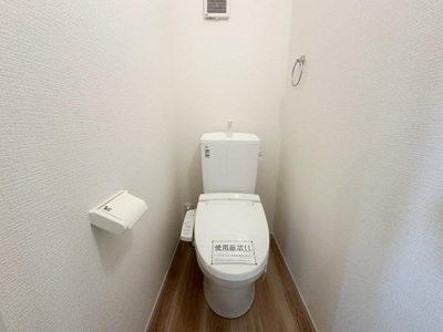 壁や床のシンプルな色合いが清潔感を演出しています。コンパクトなトイレスペースで無駄がありません。収納や設備もシンプルで使いやすい空間です。換気設備もしっかり備わっています。