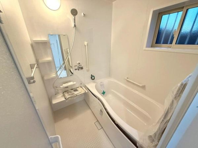 清潔感のあるバスルームです。収納棚や手すりがあり使い勝手に配慮しています。自然光が差し込む窓付きで室内は明るい雰囲気です。浴槽はゆったりとしたデザインです。手入れもしやすい仕様となっています。