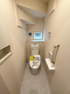 コンパクトな空間に手すりや収納スペースが設けられており利便性が感じられます。小窓があることで明るさと換気が確保されています。シンプルな内装で清潔感があります。