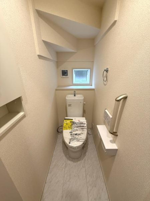 コンパクトな空間に手すりや収納スペースが設けられており利便性が感じられます。小窓があることで明るさと換気が確保されています。シンプルな内装で清潔感があります。