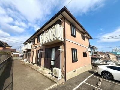 落ち着いたトーンの外観が印象的です。各住戸にはバルコニーが設けられています。建物前面には駐車スペースも確保されています。周辺には住宅が並び開放感も感じられます。空の広がりが感じられる建物です。