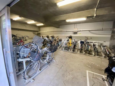 屋内に設置された自転車置き場です。ラックがあり多くの自転車を収容できるスペースが確保されています。雨風から自転車を守れる点が特徴です。出入り口が広くアクセスしやすい環境です。