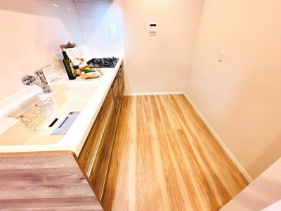 明るい色合いのフローリングが魅力のキッチンです。広々としたシンクと収納スペースを備えています。清潔感のあるデザインで整理整頓がしやすいです。壁付きのレイアウトで空間を有効に活用できます。