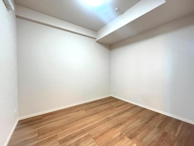 ナチュラルな色合いのフローリングが落ち着いた雰囲気を演出しています。壁や天井に凹凸が少なくシンプルな空間です。窓やドア周りもすっきりとしています。エアコン設置可能な洋室です。