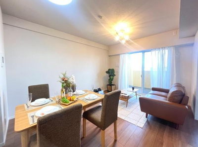 リビングは開放感のある窓から明るい日差しが入ります。テーブルやソファを配置しやすい広さです。床の色合いが空間に落ち着きを与えます。照明が天井をやさしく照らしています。室内の清潔感が感じられます。