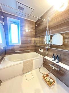 明るい採光が魅力のバスルームです。ブラウンの壁パネルが落ち着いた雰囲気を演出しています。清潔感のある床と使いやすい洗い場がポイントです。ミラーや収納棚も備わっているので便利に使えます。