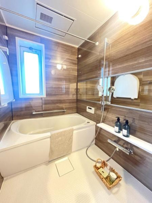 明るい採光が魅力のバスルームです。ブラウンの壁パネルが落ち着いた雰囲気を演出しています。清潔感のある床と使いやすい洗い場がポイントです。ミラーや収納棚も備わっているので便利に使えます。