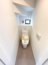 コンパクトな空間に設置されたトイレです。小窓付きで換気もしやすく清潔感のある内装が印象的です。温水洗浄便座が備え付けられており機能面にも配慮されています。壁の形状による独特な空間設計も特徴です。