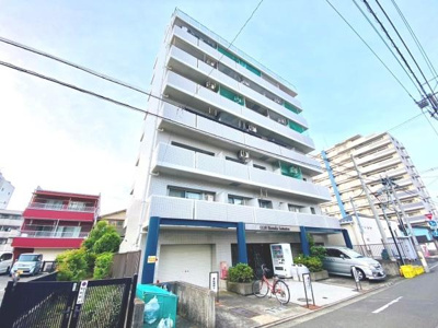 白を基調とした外観が特徴的なマンションです。エントランス周辺はすっきりと整備されています。駐車スペースも確保されています。