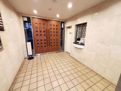 広々としたエントランスが印象的です。タイル床と木目調の扉が落ち着いた雰囲気を演出しています。受付窓口もあり安心感があります。照明が明るく清潔感が感じられます。共用部分がきちんと整備されています。