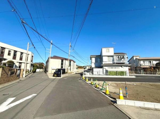 青空が広がる現地写真です。前面道路が広く車の出し入れもスムーズに行えます。周囲に住宅が整然と建ち並び落ち着いた街並みが感じられます。