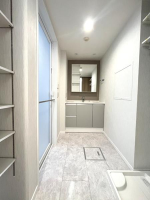 清潔感のある明るい洗面所です。広々としたスペースで鏡も大きく使い勝手が良いです。収納棚も備わっており整理しやすい設計です。床や壁の色合いも落ち着いていてシンプルな雰囲気を演出しています。