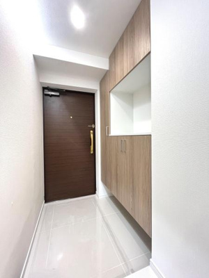 明るい照明と清潔感のある床が特徴の玄関です。シンプルなデザインで木目調の収納が玄関スペースに温かみを加えています。スッキリとした印象で日々の出入りが快適です。