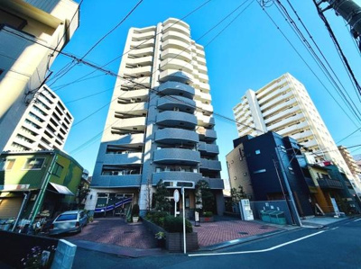 存在感のある外観が特徴の建物です。コントラストのある配色が目を引きます。周辺には建物が立ち並び都市的な雰囲気が感じられます。植栽スペースも整備され清潔感が印象的です。