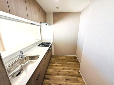 明るい色合いのフローリングが特徴的なキッチンです。シンプルなデザインでお手入れもしやすい印象です。収納スペースが上部まで設けられており整理整頓もしやすそうです。作業台もすっきりまとまっています。