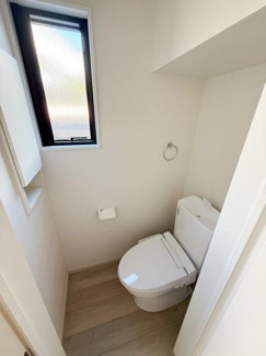 窓付きで採光と換気が確保されたトイレです。清潔感のある白基調の空間が印象的です。使いやすいレイアウトで快適にご利用いただけます。床材も落ち着いた色合いでまとまっています。収納スペースも備わっています。